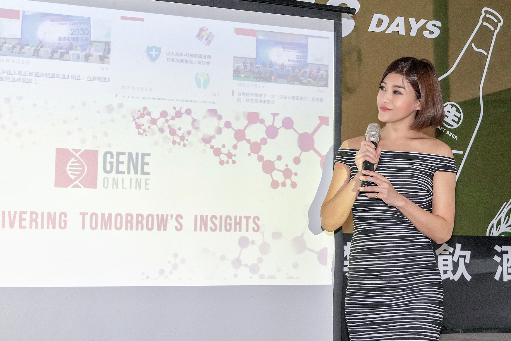 主持人 Yuki Hsu 在「基因線上」5週年晚會上，於簡報螢幕前專注聆聽，展現沉穩專業的控場能力。