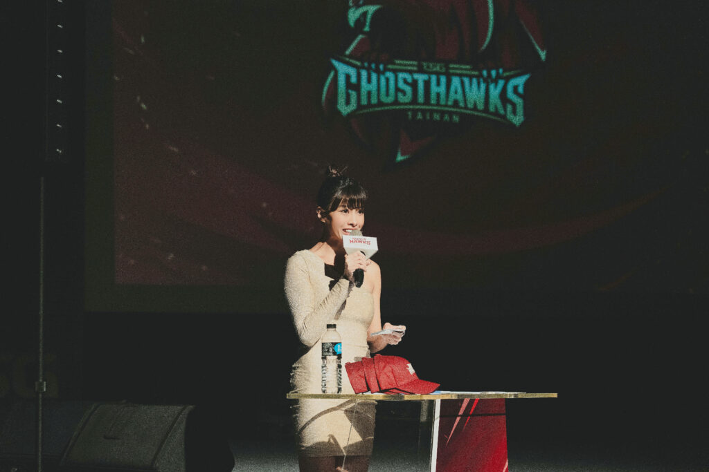 在燈光聚焦的舞台上,主持人Yuki面帶微笑、眼神專注地手持麥克風主持,展現出專業與自信。