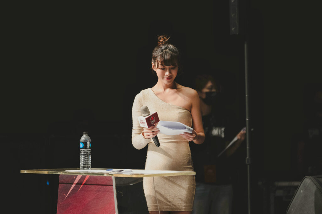 在活動進行中,主持人Yuki在舞台上低頭專注地看著手中的流程卡,展現其對細節一絲不苟的專業態度。