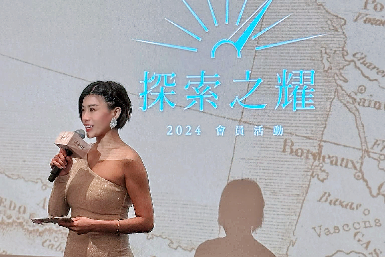 中英主持人 Yuki 在酒如坊「探索之耀」品酒會上，一邊手持講稿，展現其卓越的現場互動與氣氛營造能力。